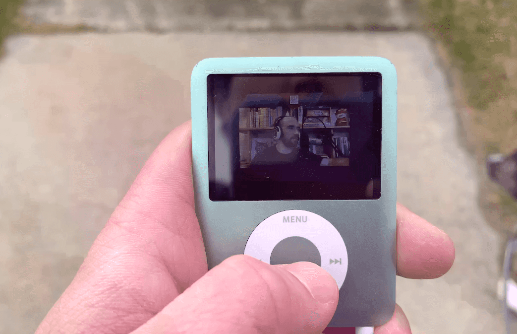 A close-up photo of a hand holding an iPod nano which is playing a video