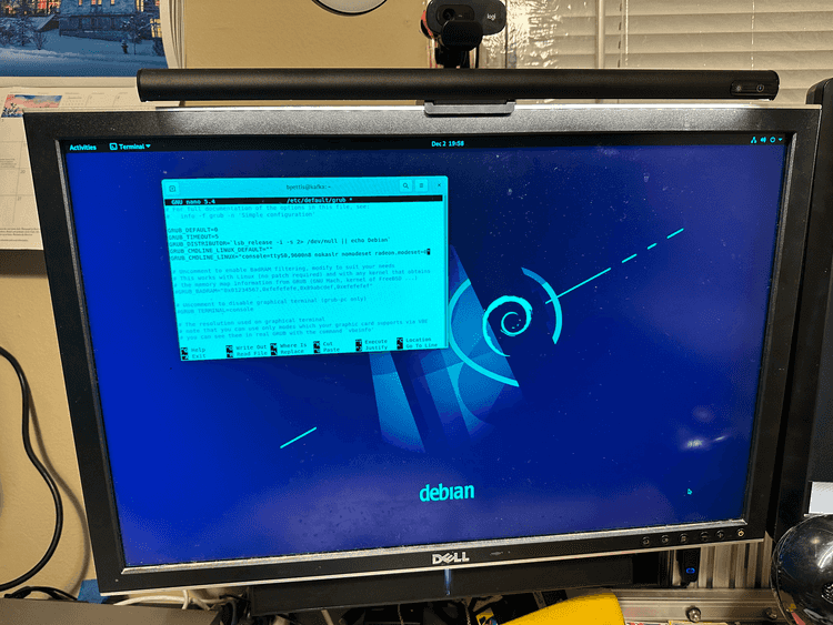 A photo of a computer monitor. On screen we see an installation of Debian 11 with the default background. There is a terminal window open that is editing a GRUB config file